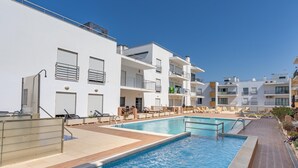 A rooftop pool area with multiple swimming pools, lounge chairs, and a clear blue sky.