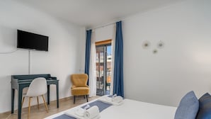 A hotel room with a bed, a desk, a chair, a TV, and a view of the outside.
