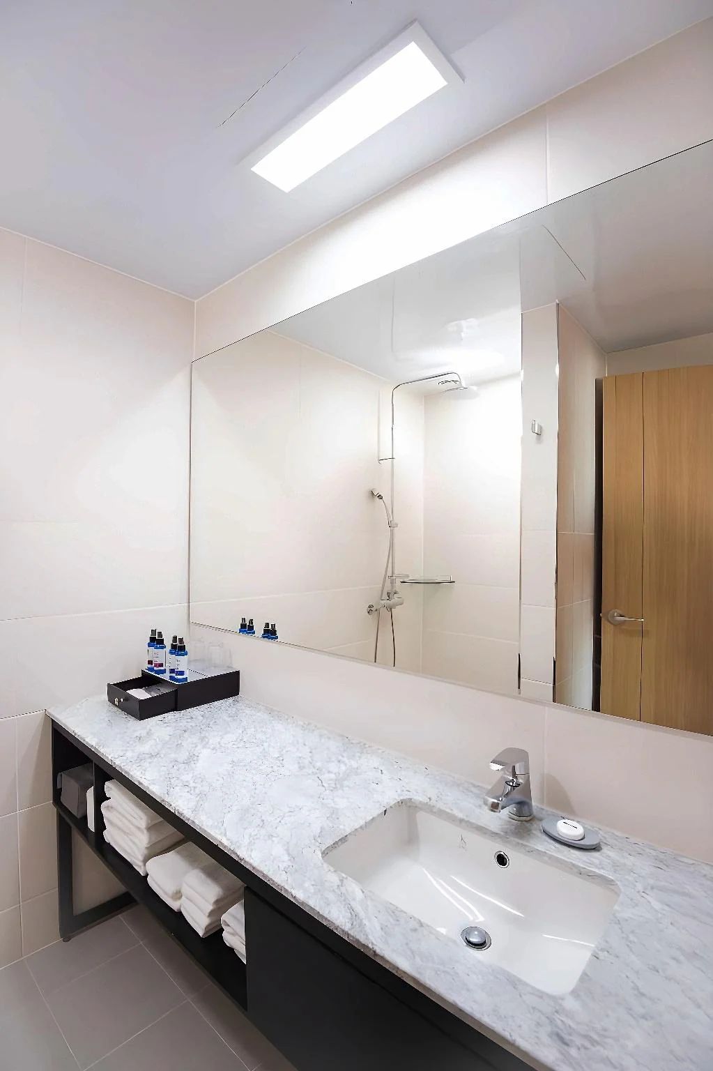 A modern bathroom with a large mirror, a white sink, and a shower.
