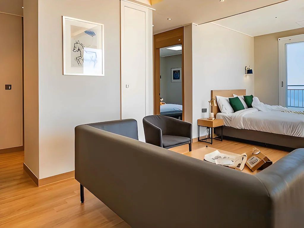 Une chambre d’hôtel moderne équipée d’un lit, d’un canapé, d’une chaise, d’une table de chevet et d’un miroir.