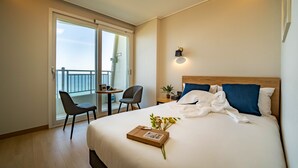 A hotel room with a large bed, a desk with a chair, a balcony with a view, and a wall-mounted light fixture. - PINEART LABEL (Gangneung)
