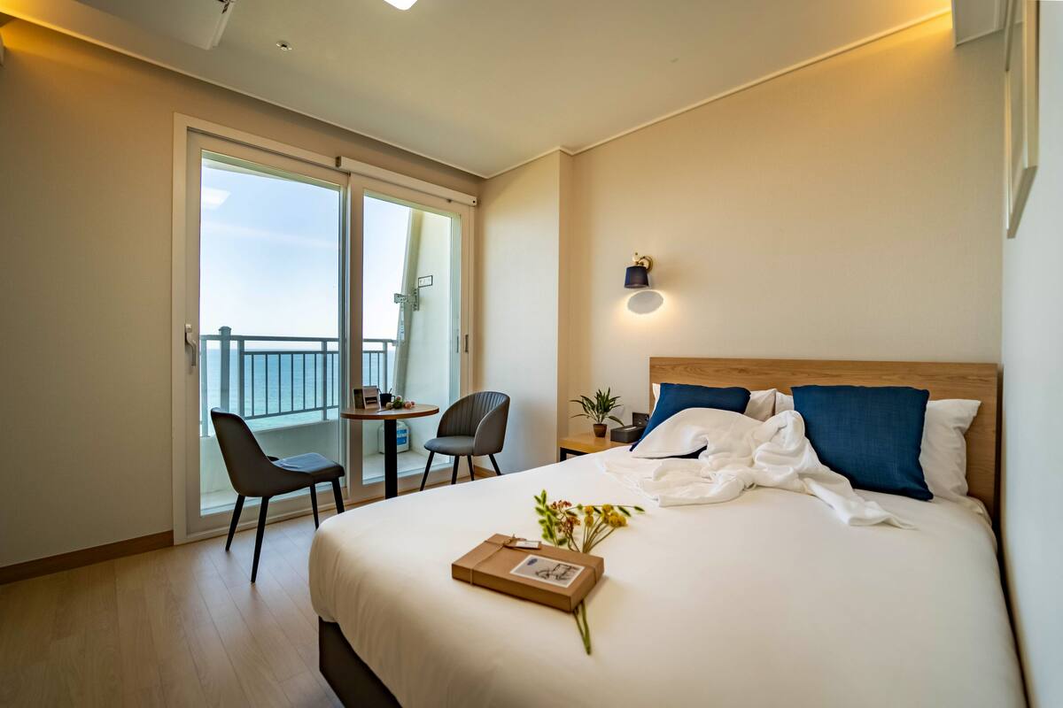 Habitación de hotel con una cama grande, un escritorio con silla, un balcón con vistas y una lámpara fijada a la pared.