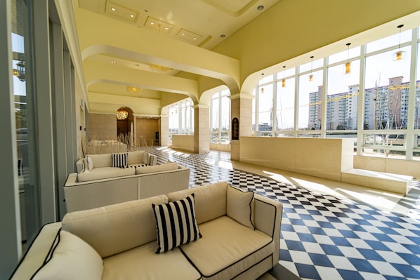 A spacious lobby with a checkered floor, large windows, and a seating area with a sofa and armchairs.