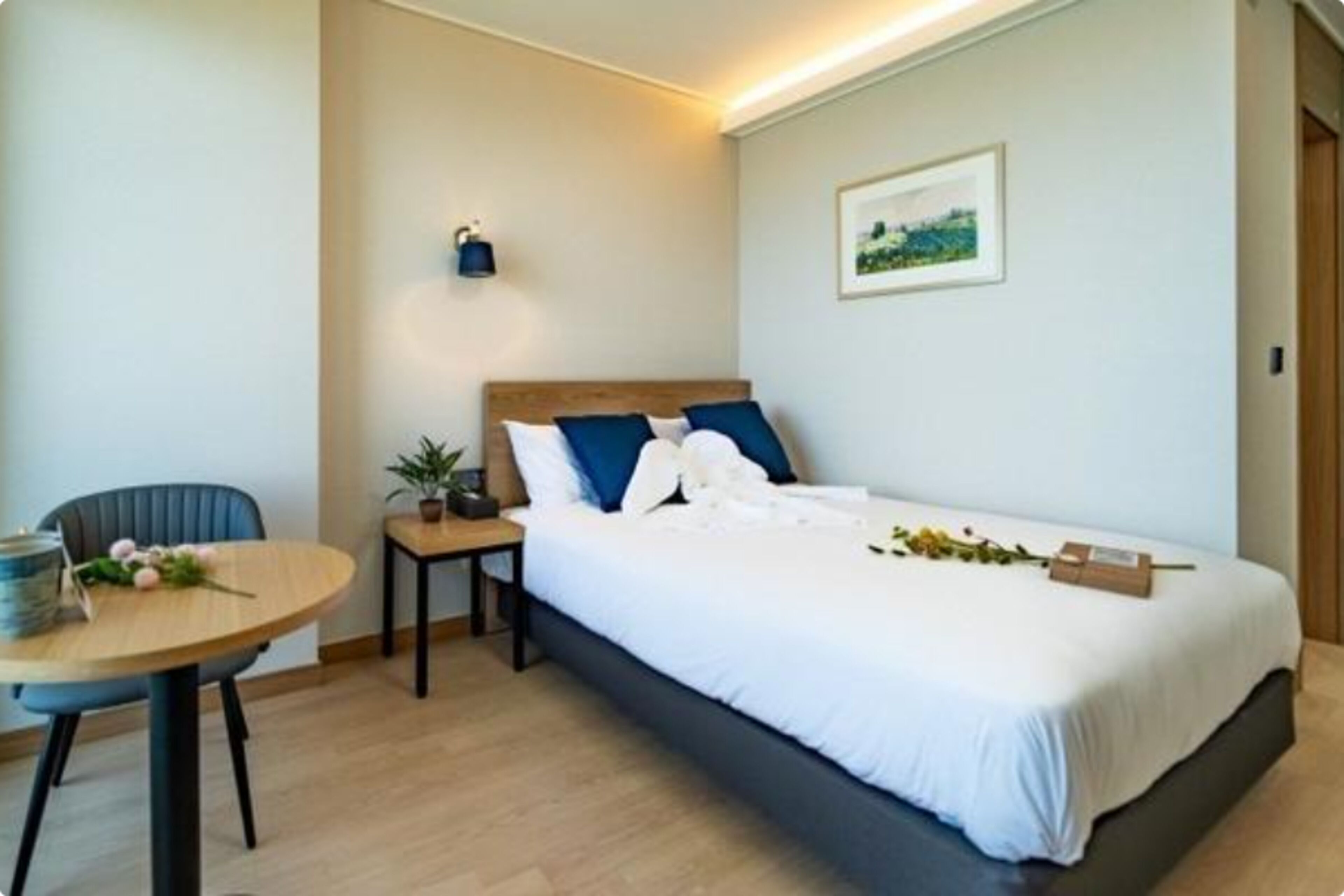 A modern bedroom with a bed, bedside table, chair, and a small table with a plant.