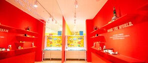 Una stanza luminosa con pareti rosse, scaffali con diversi oggetti e un tavolo centrale con un cartello giallo.
