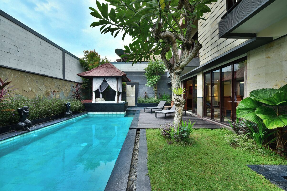 A modern outdoor pool area with a small gazebo, a well-maintained lawn, and a stone wall.