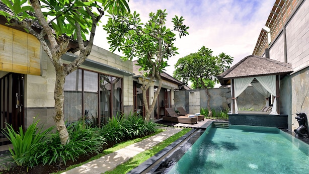 A swimming pool with a stone-lined edge, surrounded by a garden with various plants and a tree. - The Khayangan Dreams Villa Seminyak  (Seminyak)