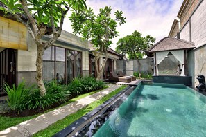 A swimming pool with a stone-lined edge, surrounded by a garden with various plants and a tree. - The Khayangan Dreams Villa Seminyak  (Seminyak)