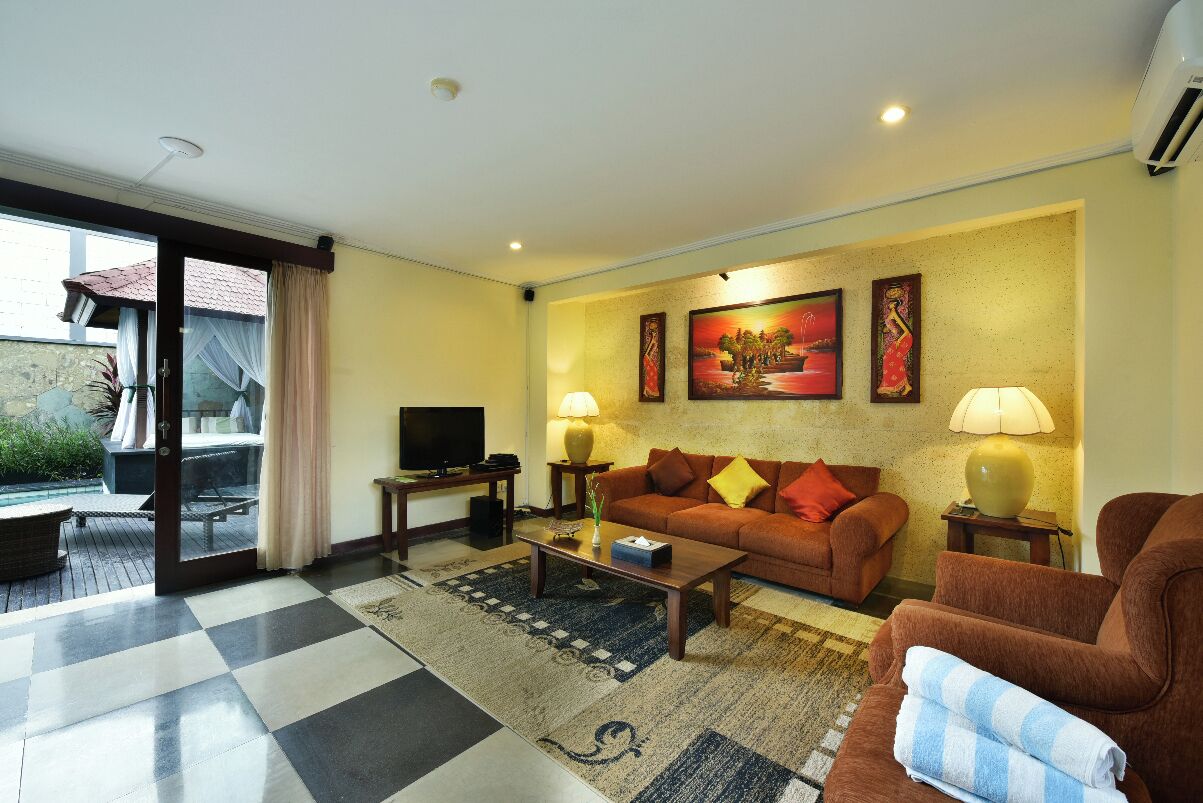 A living room with a sofa, coffee table, and two lamps. There is a television on a stand and a window with curtains.