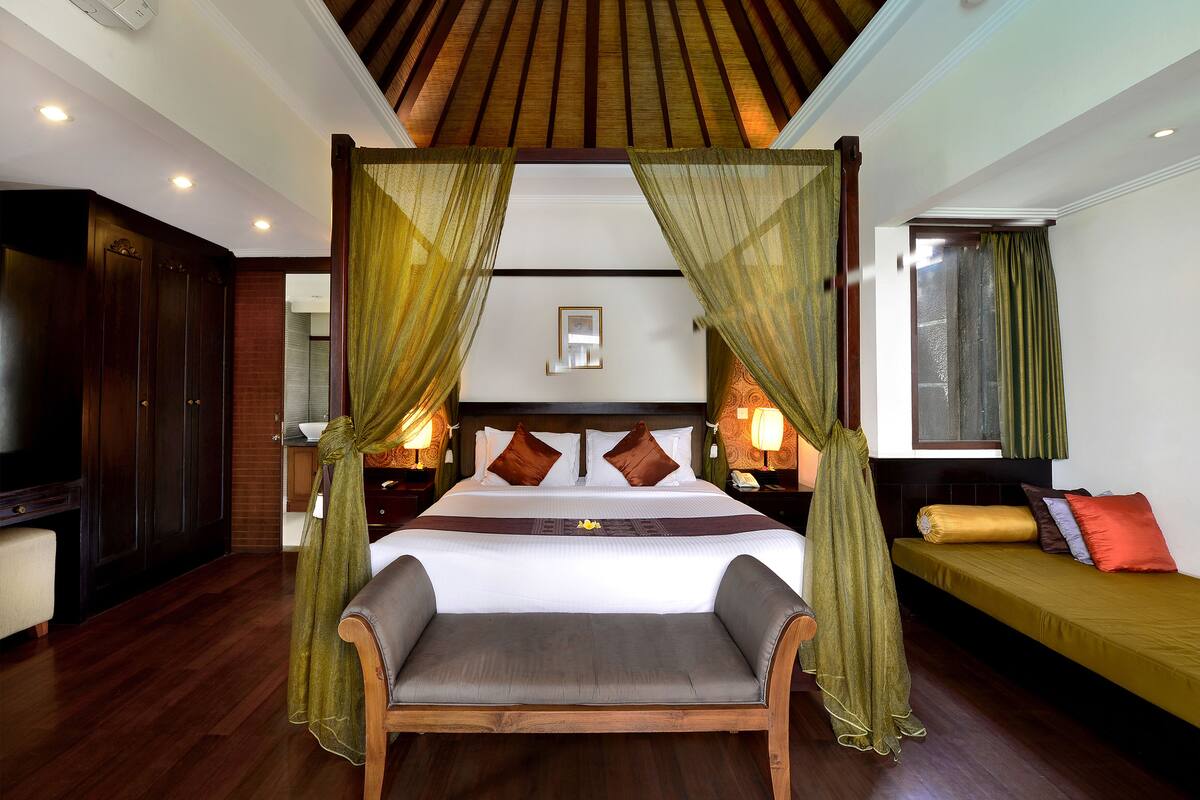 A bedroom with a four-poster bed, a bench, a sofa, and a TV.