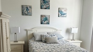 A bedroom with a bed, two bedside tables, a ceiling fan, and four wall-mounted artworks. - Cheerful & Vibrant Home Near Mineral Springs (North Port)