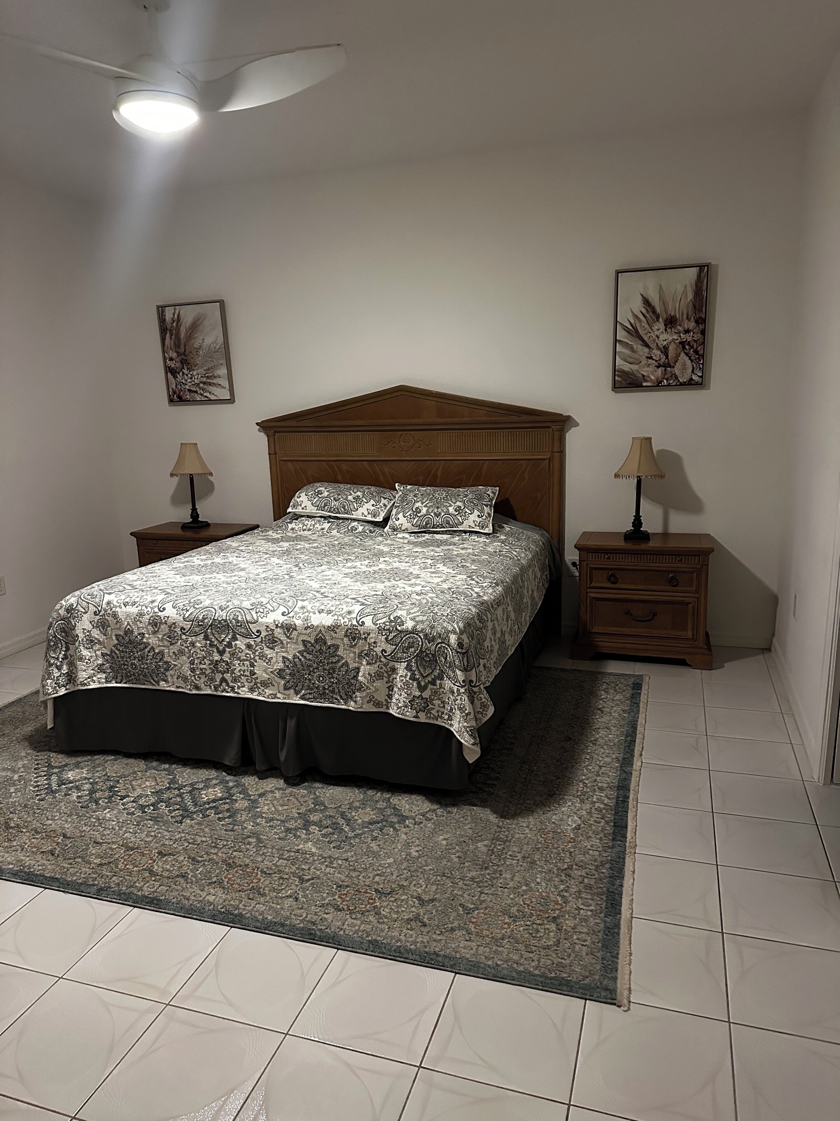 A bedroom with a bed, nightstands, a ceiling fan, and two wall-mounted lamps.