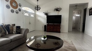A living room with a sofa, a round table, a TV, and decorative plates on the wall. - Cheerful & Vibrant Home Near Mineral Springs (North Port)