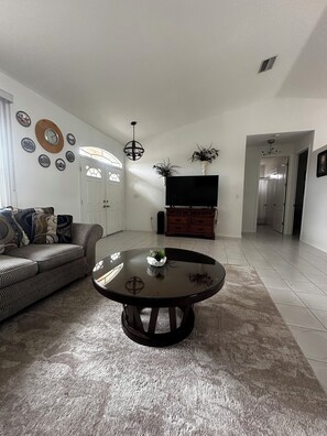 A living room with a sofa, a round table, a TV, and decorative plates on the wall. - Cheerful & Vibrant Home Near Mineral Springs (North Port)
