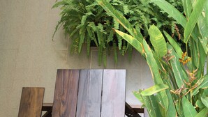 Un banco de madera con estructura metálica, ubicado frente a una pared con ventana y planta colgante.
