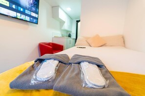 Una habitación de hotel con cama, televisor montado en la pared y una silla roja.