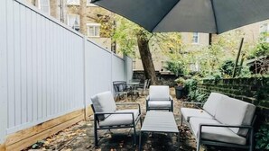 Une terrasse extérieure avec une table et quatre chaises, entourée d’une clôture blanche et d’un arbre.