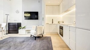 Une cuisine moderne avec des armoires blanches, un four encastré et un four à micro-ondes. Un tapis gris recouvre le sol et une chaise blanche se trouve dans l’espace salon.
