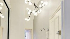 Un couloir doté d’un lustre moderne, de murs blancs et d’un plancher en bois.