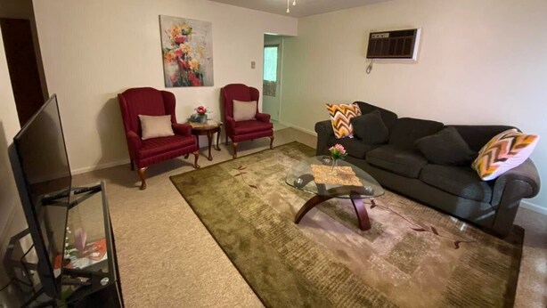 Een woonkamer met een plafondventilator, twee rode fauteuils, een zwarte bank, een glazen salontafel en een tv-meubel.