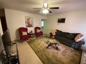 A living room with a ceiling fan, two red armchairs, a black sofa, a glass coffee table, and a TV stand. - 2mins from Miami U, Cozy duplex home (Oxford)