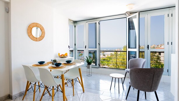 Un comedor moderno con una mesa blanca, sillas amarillas y vistas de la ciudad a través de amplias ventanas.