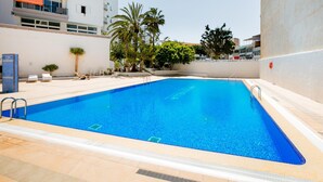 Una piscina con agua cristalina azul, rodeada por un deck con baldosas y una pared blanca.