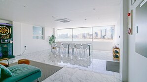 A modern, well-lit room with a large window offering a city view, a dartboard, and a seating area with chairs and a sofa. - The Wave Pension (Busan)