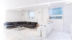 A modern living room with a sectional sofa, a coffee table, and a kitchen area with a microwave. - The Wave Pension (Busan)