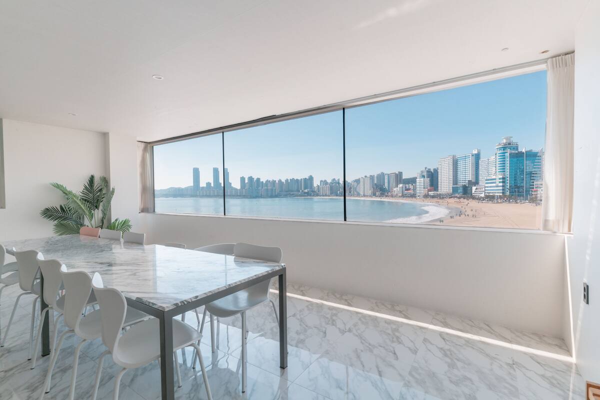 A modern room with a large window overlooking a beach and city skyline.