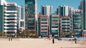 A cityscape with modern buildings, including a hotel named "Q-MOTEL" and various other commercial establishments. - The Wave Pension (Busan)