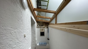 A narrow, white-walled room with a sloped ceiling, a small bench with a striped cushion, and a stone wall with a picture frame.