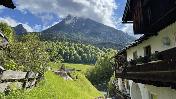 A mountain view with a wooden house and a balcony with potted plants.