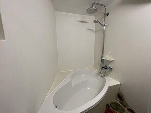 A bathroom with a white bathtub, a showerhead, and a small shelf.