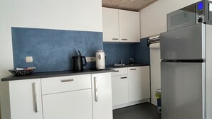 A modern kitchen with white cabinets, a black countertop, a stainless steel refrigerator, and a blue accent wall.