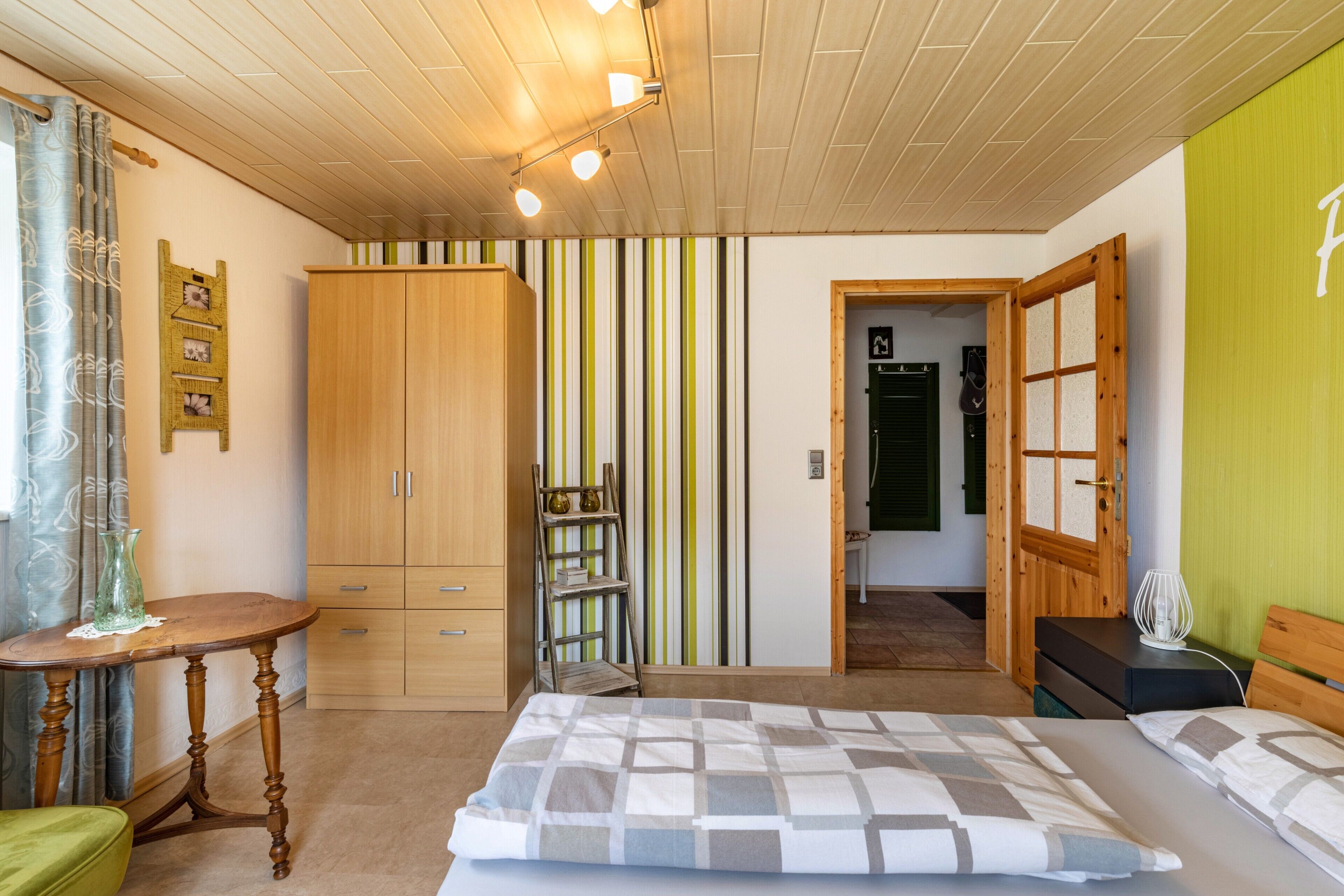 A bedroom with a bed, wooden wardrobe, a small table, and a chair.