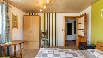 A bedroom with a bed, wooden wardrobe, a small table, and a chair.