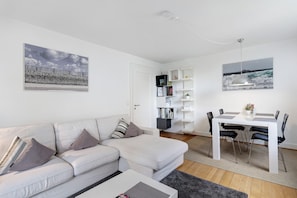 Un salon moderne avec un canapé blanc, une table à manger avec des chaises et deux œuvres d’art accrochées au mur.