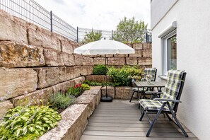 Une terrasse avec une table et des chaises, un parasol blanc et un mur en pierre.