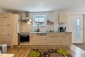 Une cuisine moderne avec des meubles en bois, un four encastré, une fenêtre et une machine à café.