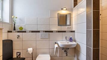 A bathroom with a toilet, sink, mirror, and towel rack.