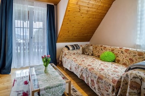 Une chambre à coucher confortable aménagée en mezzanine, avec un plafond en bois, un canapé à motifs floraux, un coussin vert, un vase rempli de fleurs et un tapis à motifs.