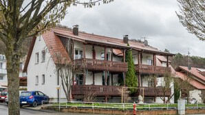 Un edificio de dos pisos con balcón, techo rojo y fachada blanca.