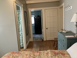 A bedroom with a bed, a dresser, a lamp, and a door leading to a kitchen. - One-Bedroom Apt in Hampton NH! (Hampton)