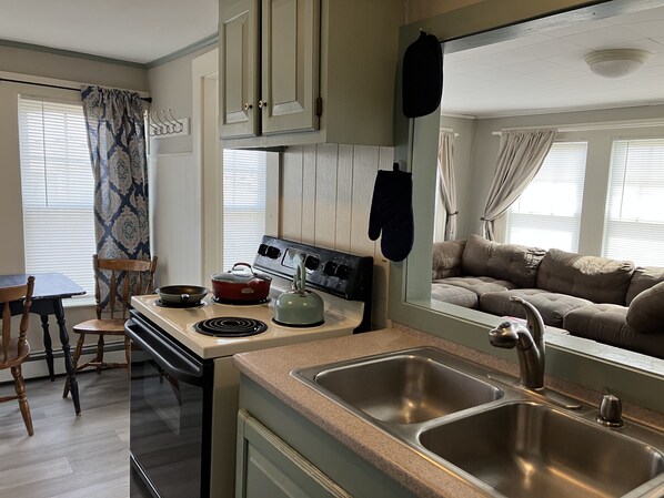 A compact kitchen with a stove, sink, and a dining area with a table and chairs. - One-Bedroom Apt in Hampton NH! (Hampton)