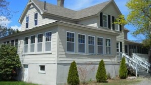 A two-story house with a front porch, a chimney, and a staircase leading to the entrance. - One-Bedroom Apt in Hampton NH! (Hampton)