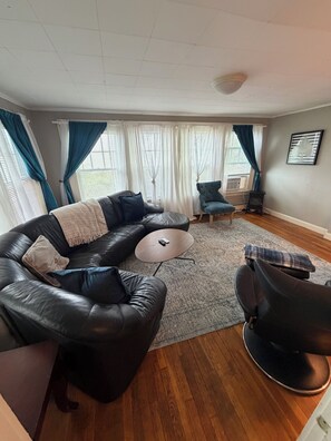 A living room with a sectional sofa, a round coffee table, a blue armchair, and a rug. - One-Bedroom Apt in Hampton NH! (Hampton)