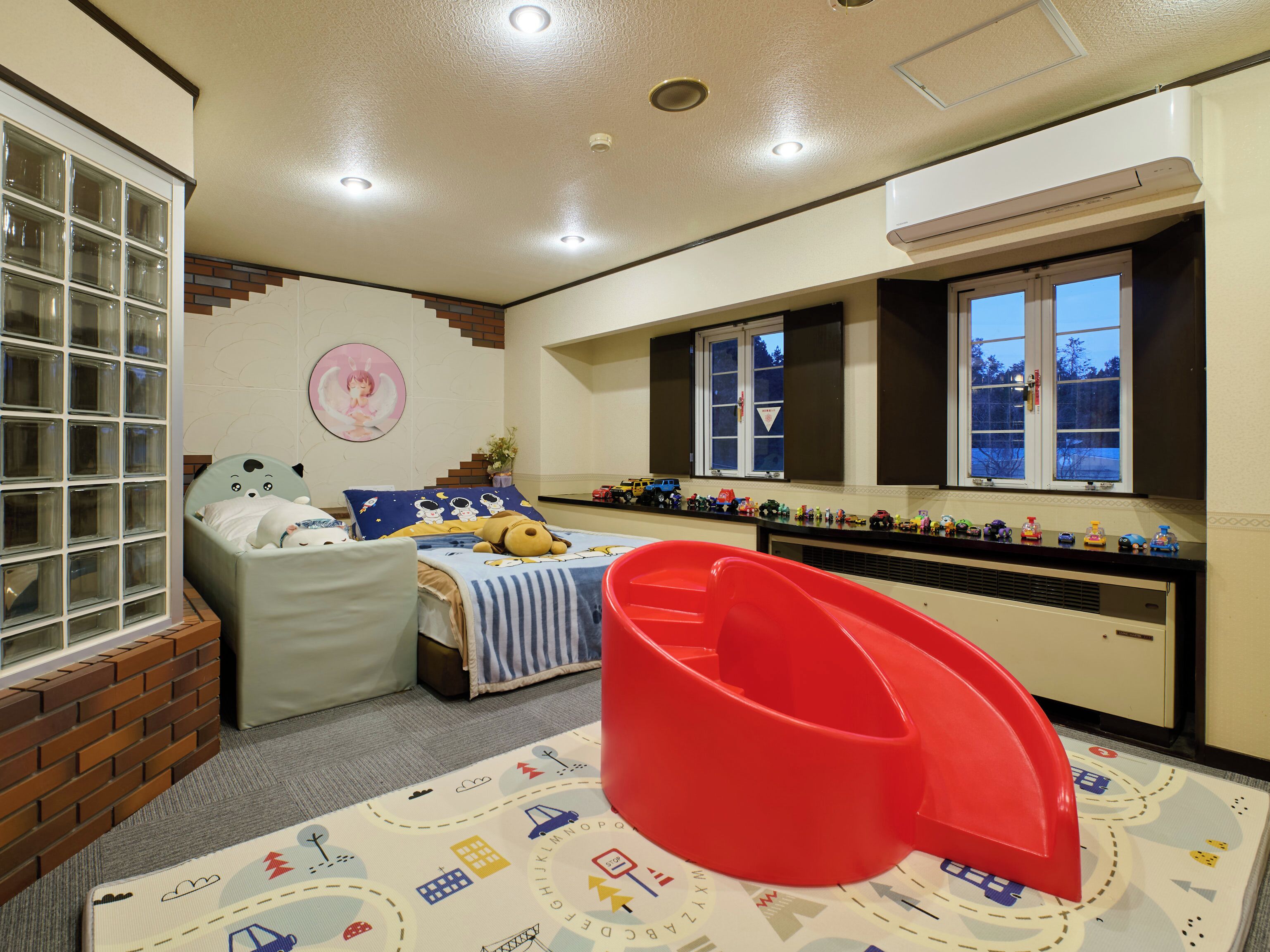 A child's bedroom with a bed, a red slide, a window, and a toy train display.