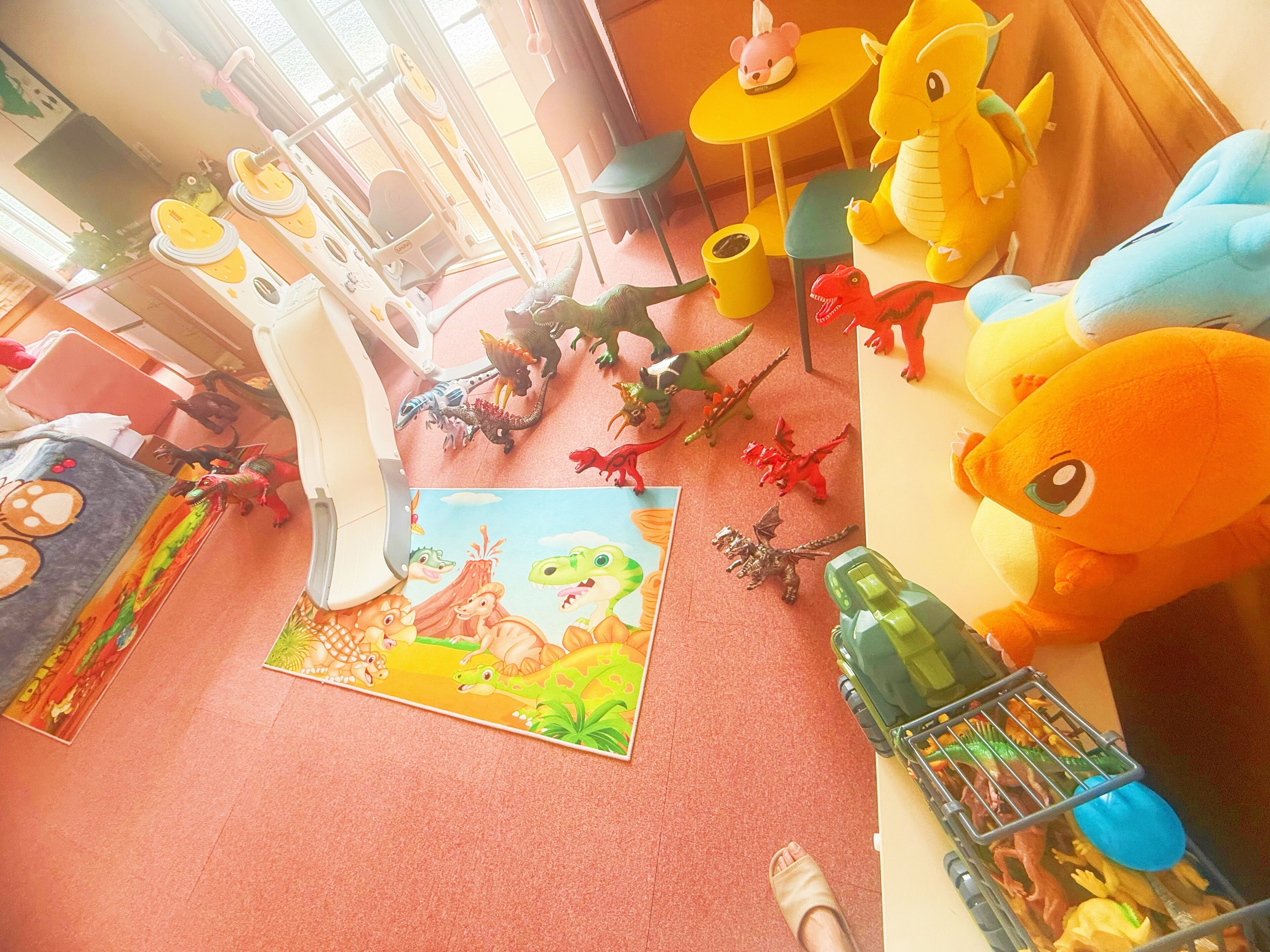 A room with a red carpet, a dinosaur-themed rug, a toy car, and a large plush toy.