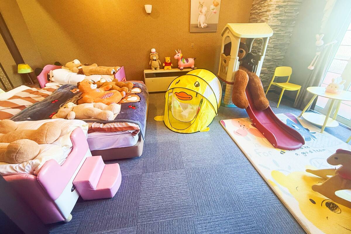 A child's bedroom with a bed, stuffed animals, a play tent, and a slide.
